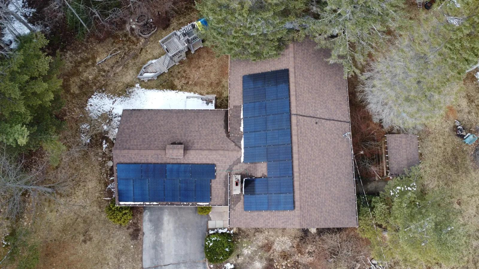 Overhead view of a Lower Coverdale, New Brunswick home with solar panels across two roof faces, set among evergreens.
