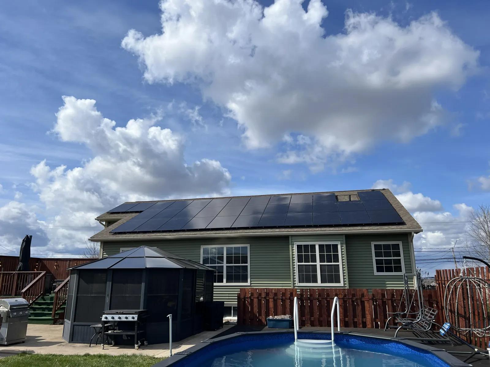 Rear view of a Riverview, New Brunswick home with a full run of black solar panels along the roofline, overlooking a backyard pool.