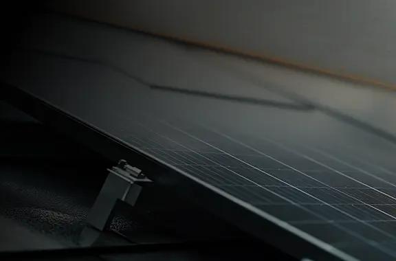 Close-up of a solar panel secured to a roof by an anodized aluminum racking clamp.