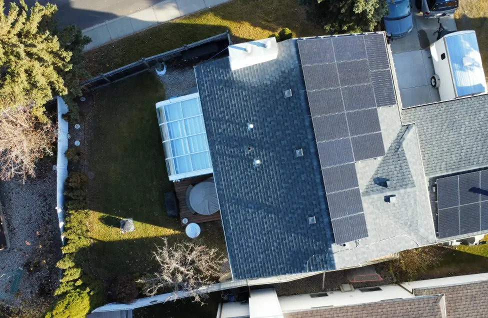High-angle aerial view of a professional residential solar panel installation on a grey shingled roof in Alberta, featuring sleek, high-efficiency black panels.